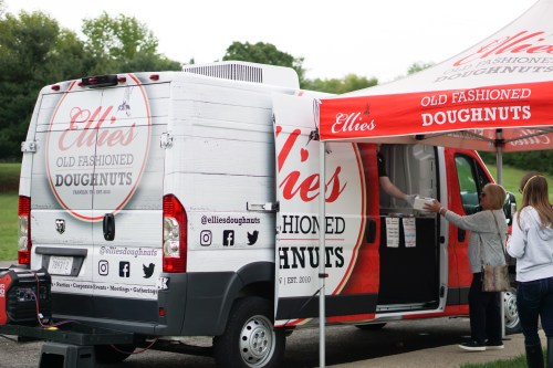 A food truck with "Ellie's Old Fashioned Doughnuts" signage, serving customers under a matching tent.