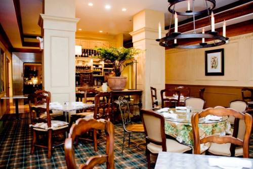 Cozy restaurant interior with wooden tables, chairs, and a potted plant, featuring warm lighting and a checkered floor.
