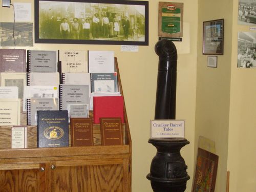 A display featuring books and historical photos, with a black stove pipe labeled "Cracker Barrel Tales" in the foreground.