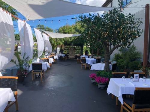 Outdoor dining area with white tablecloths, potted plants, and draped fabric, creating a cozy atmosphere.