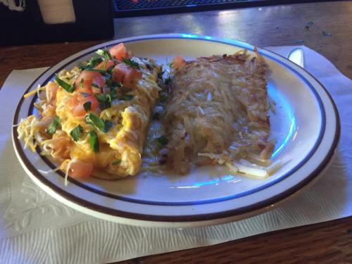 A plate with a cheesy omelette topped with tomatoes and herbs, alongside crispy hash browns.