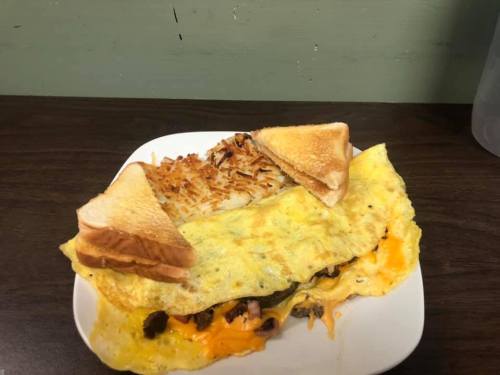 A plate with a large omelette filled with cheese and meat, served with hash browns and two slices of toast.