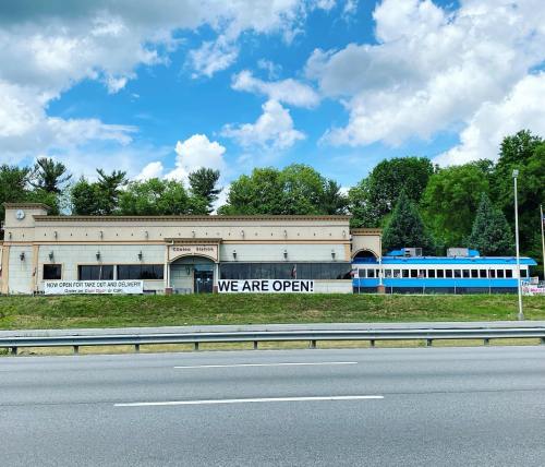 A restaurant building with a sign reading "WE ARE OPEN!" and a blue train parked nearby, set against a cloudy sky.