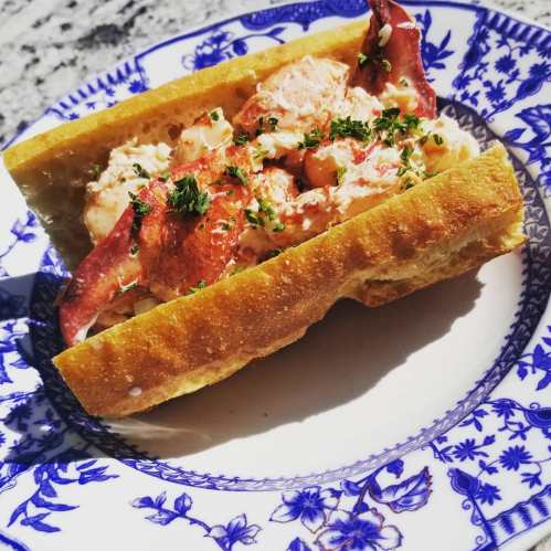A lobster roll filled with lobster meat, garnished with herbs, served on a decorative blue and white plate.