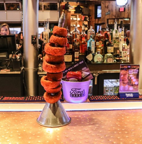 A tower of stacked donuts on a metal cone, with a bar and bottles in the background.