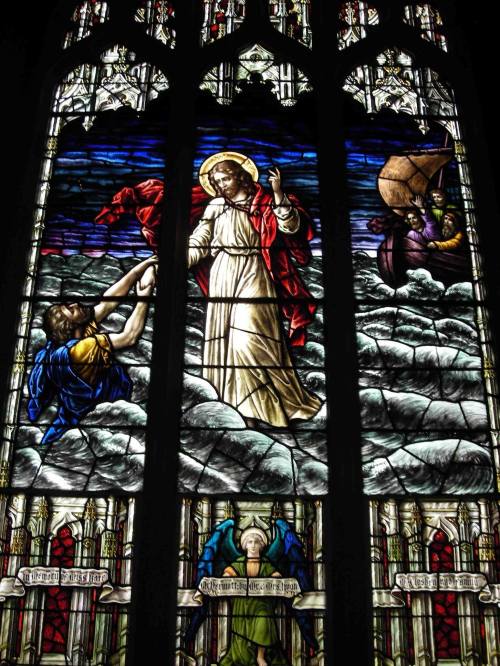 Stained glass window depicting Jesus walking on water, with disciples and a boat in a stormy sea.