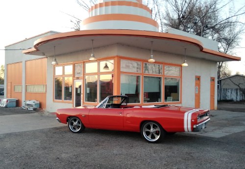 A bright red convertible parked in front of a retro-style building with orange accents and large windows.
