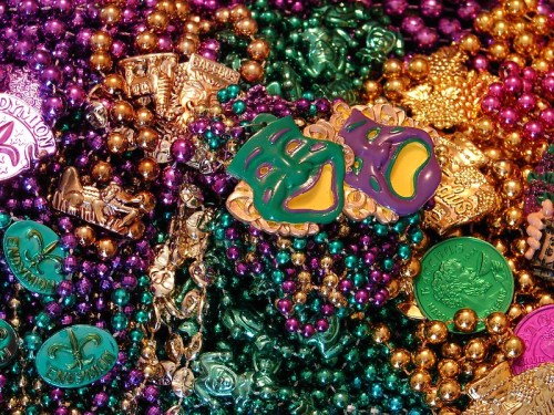 A colorful assortment of Mardi Gras beads and tokens, featuring purple, green, and gold hues with decorative masks.