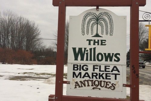 Sign for "The Willows" featuring a big flea market and antiques, surrounded by snow and bare trees.
