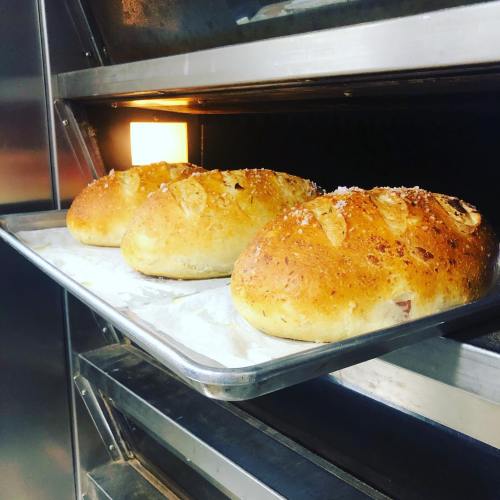 Three freshly baked loaves of bread on a tray, resting in an oven with a warm glow.