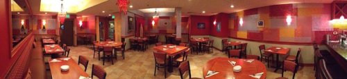 A spacious restaurant interior with wooden tables, chairs, and colorful wall decor, featuring warm lighting.