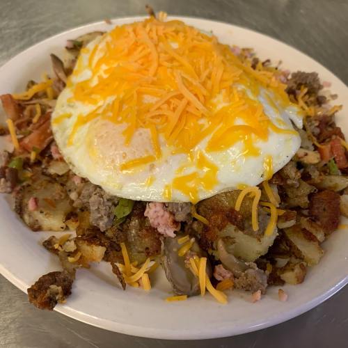 A plate of hash browns topped with ground meat, diced vegetables, and a sunny-side-up egg, garnished with shredded cheese.