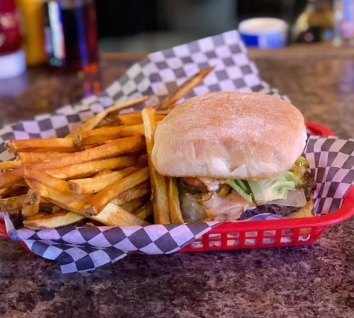 A burger with lettuce and toppings served with a side of golden French fries in a red basket with checkered paper.