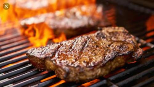 Juicy steaks sizzling on a grill with flames in the background, showcasing a delicious barbecue scene.