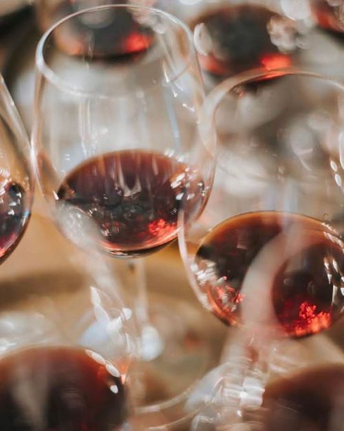 A close-up of several wine glasses filled with red wine, creating a blurred, artistic effect.