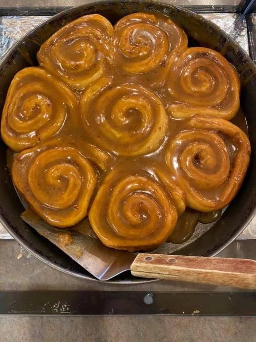 A freshly baked cinnamon roll cake with a glossy caramel glaze, arranged in a circular pattern in a baking pan.