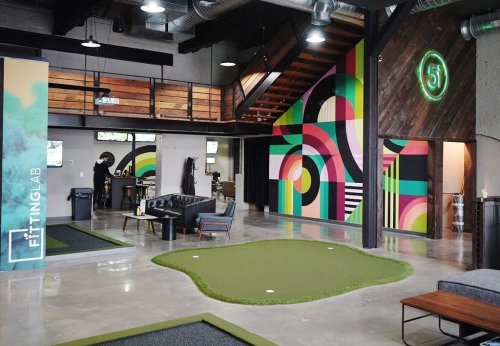 A modern indoor space featuring a putting green, colorful wall art, and stylish seating areas.