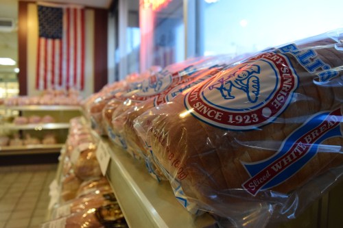Bags of sliced white bread on a shelf, with an American flag in the background.