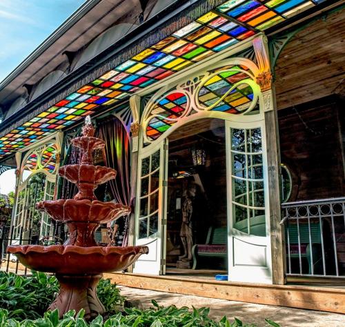 A colorful stained glass awning above a fountain in front of a charming wooden building with open doors.