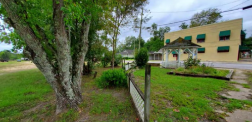 A grassy area with trees, a gazebo, and a building with green awnings in a quiet, rural setting.