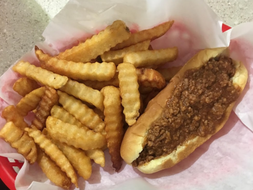 A plate with crinkle-cut fries and a chili dog in a red basket lined with pink paper.