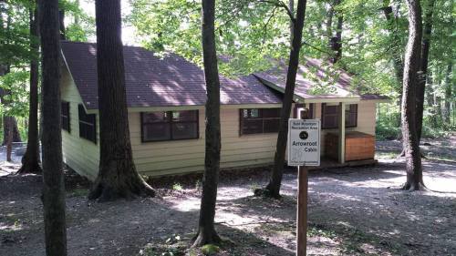 A cabin surrounded by trees in a wooded area, with a sign indicating "Arrowroot Cabin" in front.