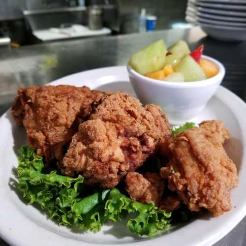 A plate of crispy fried chicken pieces on a bed of lettuce, served with a side of fresh fruit salad.