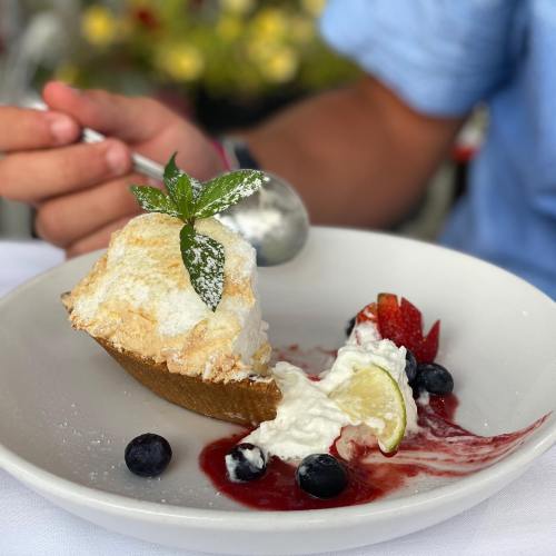 A dessert with a meringue topping, whipped cream, berries, and a slice of lime on a white plate.