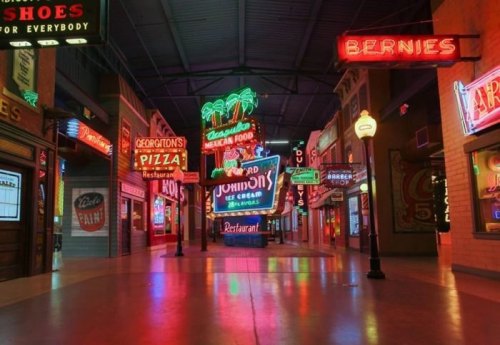 A vibrant indoor street scene filled with colorful neon restaurant signs and vintage storefronts.