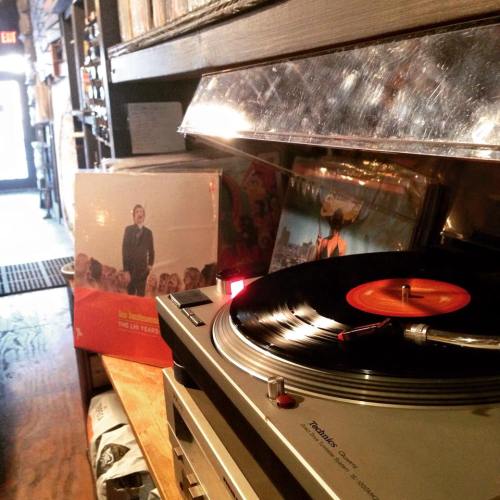 A record player with a vinyl spinning, next to an album cover in a cozy music shop.