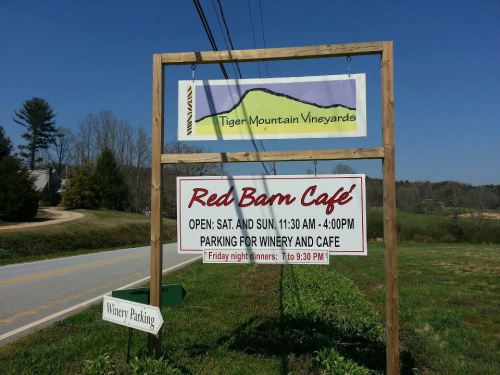 Sign for Tiger Mountain Vineyards and Red Barn Café, with details on hours and parking information. Scenic rural backdrop.