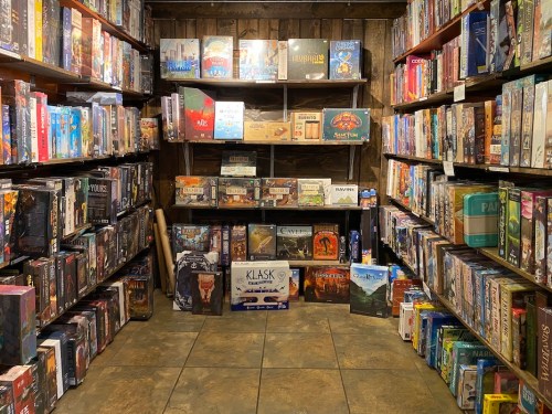 A cozy game store filled with shelves of board games, featuring various titles and colorful boxes.