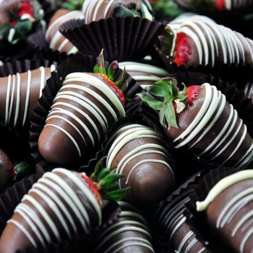 A close-up of chocolate-covered strawberries arranged in decorative cups, drizzled with white chocolate.