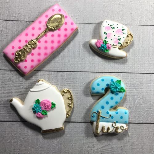 Decorative cookies shaped like a teapot, teacup, spoon, and the number "2," all with floral designs and pastel colors.