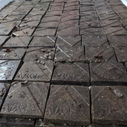 A close-up of dark, textured tiles arranged in a geometric pattern, some covered with small debris.