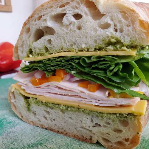 A cross-section of a sandwich with turkey, cheese, lettuce, and pesto on thick, crusty bread.
