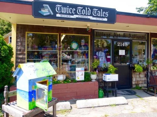 A quaint bookstore with a colorful display of books and gifts outside, featuring a small painted birdhouse.