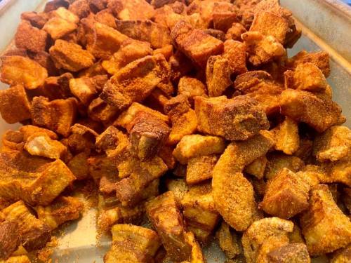 A close-up of crispy, seasoned pork cracklings piled on a tray.