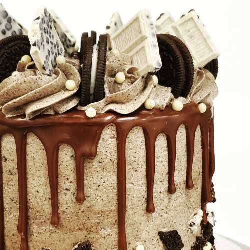 A decadent chocolate cake topped with swirls of frosting, Oreo cookies, and chocolate bars, with a glossy drip effect.