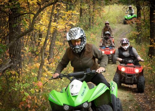A group of people riding ATVs on a forest trail surrounded by autumn foliage.