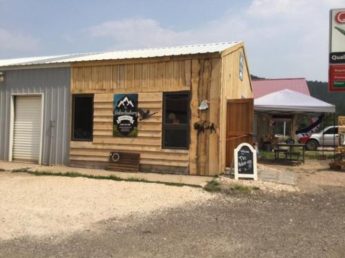 A rustic wooden building with a sign, surrounded by gravel and a tent, set against a cloudy sky.