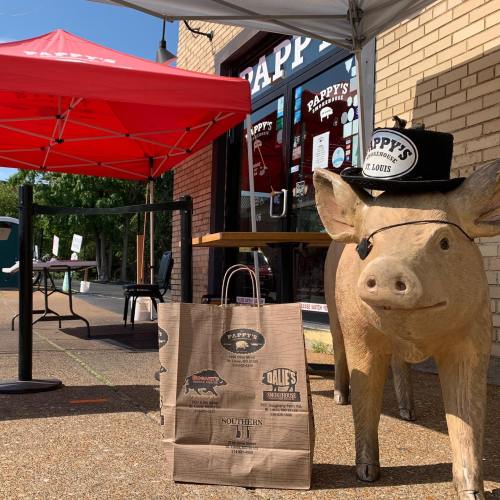 A pig statue wearing a hat stands next to a branded bag outside Pappy's restaurant under a red canopy.
