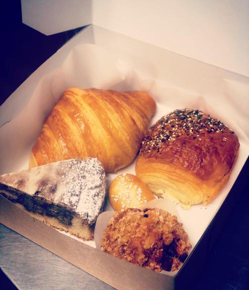 A box of assorted pastries including a croissant, danish, cake slice, and sweet rolls, arranged neatly on parchment paper.