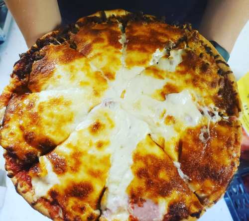 A freshly baked pizza with melted cheese and a golden crust, cut into slices and held by hands.