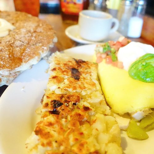 A plate featuring a large pancake, hash browns, and a colorful omelet with toppings, alongside a small cup of coffee.