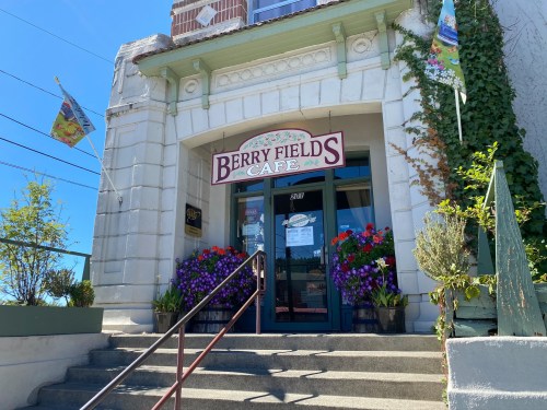 Entrance of Berry Fields Café with colorful flowers and flags, featuring a welcoming sign and steps leading up.