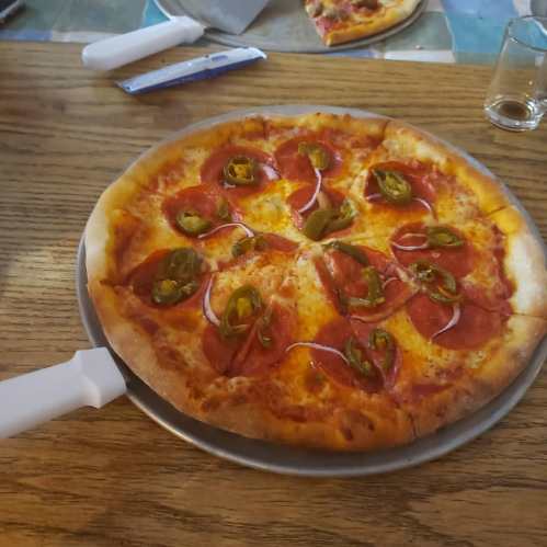 A pizza topped with pepperoni and jalapeños on a wooden table, with a pizza cutter beside it.