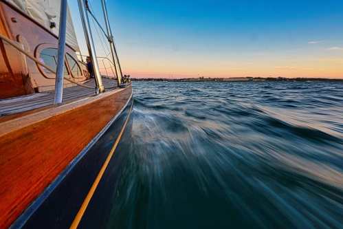 A close-up of a boat's side cutting through water at sunset, with a vibrant sky in the background.