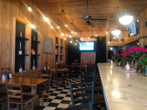 Cozy restaurant interior with wooden walls, checkered floor, and a bar adorned with flowers and soft lighting.
