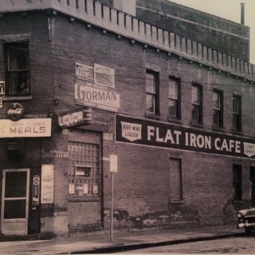 Black and white photo of a brick building featuring signs for Flat Iron Cafe and Gorman County.